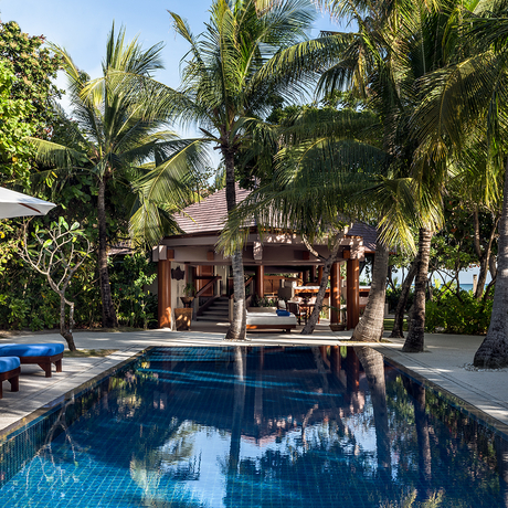 Swimming pool at Amanpulo surrounded by palm trees and tropical gardens, with villa structures in the background.