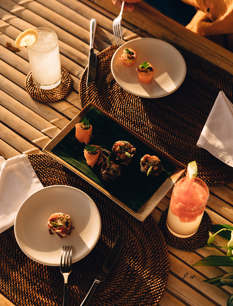 Amanpulo dining setup with plated courses, cocktails, and table settings arranged on wooden decking.