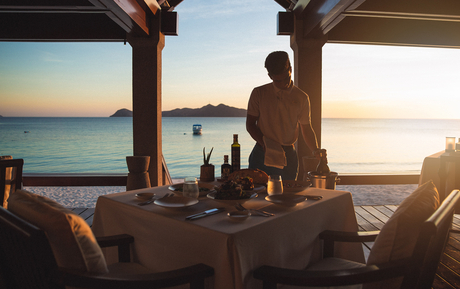 Woman standing at a beachfront dining pavilion at Amanpulo at sunset, overlooking the sea.