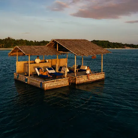 Wooden outrigger boat with golden-toned shelter moored in clear blue waters at Amanpulo.