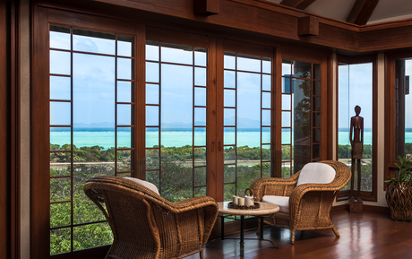 Amanpulo villa interior with floor-to-ceiling windows overlooking tropical landscape and ocean beyond.