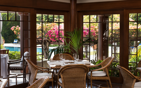Amanpulo dining pavilion with wooden doors opening to tropical gardens and ocean views.