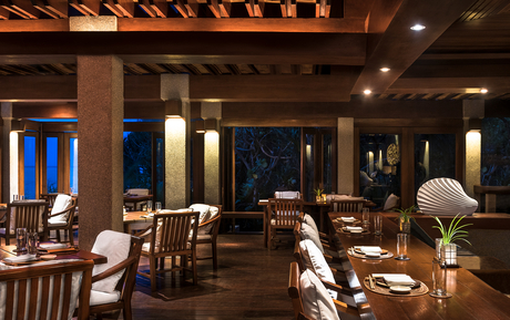 Amanpulo dining venue with wooden beams, floor-to-ceiling windows overlooking the ocean at dusk, and elegantly arranged tables.