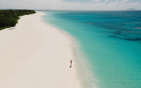 Aerial view of a white sand beach and turquoise waters at Amanpulo, with a solitary figure standing on the shore.