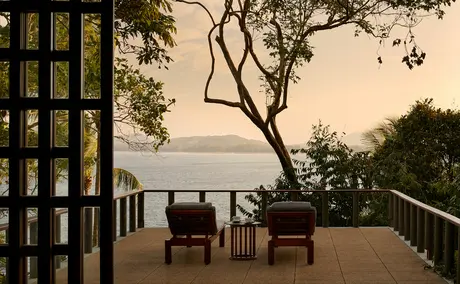 Wooden chairs on a teak deck at Amanpuri overlooking tropical waters at dusk.