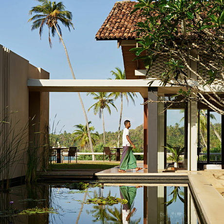 Amanwella villa with wooden pergola overlooking reflecting pool and palm trees.