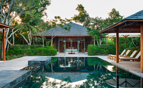 Amanyara villa with central pool, wooden pergola, and lush tropical gardens at sunset.