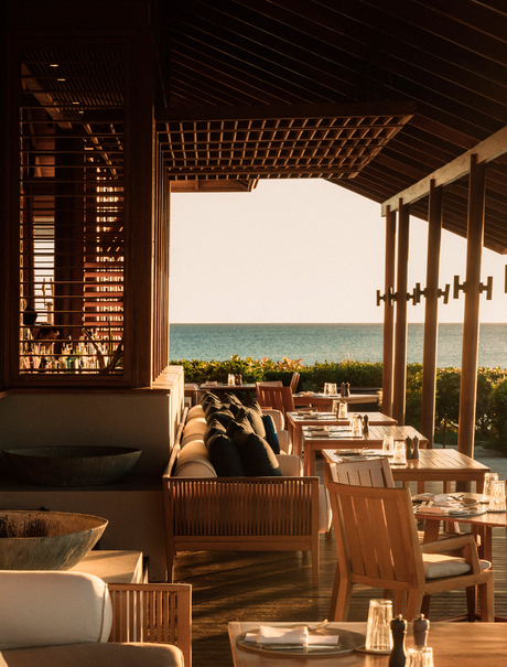 Dining venue at Amanyara with wooden screens and chairs overlooking turquoise waters at sunset.