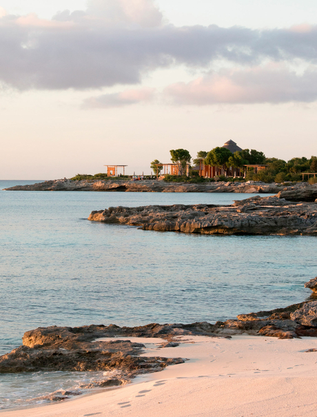 Amanyara's sandy shoreline meets turquoise waters at dusk, with rocky outcrops along the tropical coast.