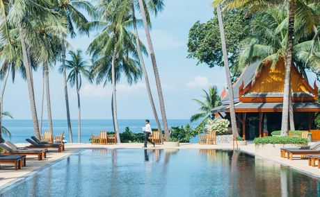 Main pool at Amanpuri overlooking the Andaman Sea, Thailand, with wooden loungers and tropical palms.