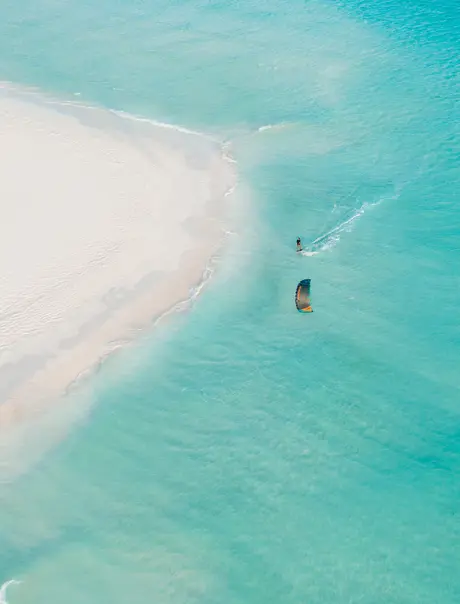 Kite surfer gliding across turquoise waters near white sand beach at Amanpulo resort.