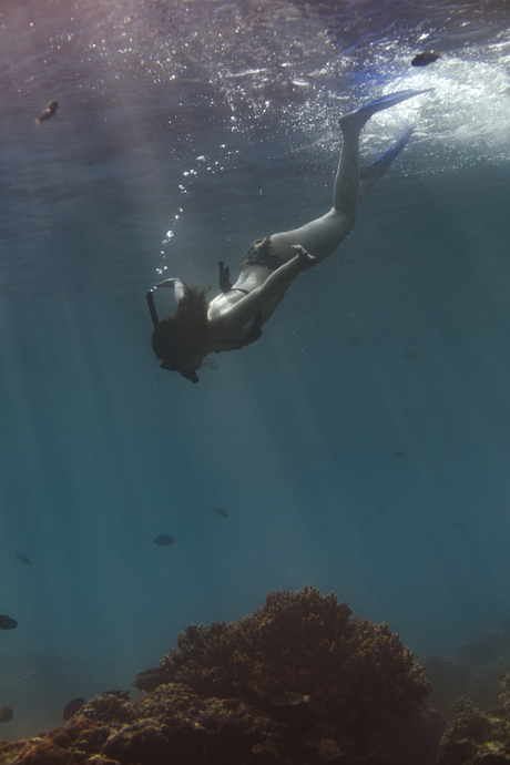 Snorkeller diving towards coral reef in clear blue waters at Amankila, Bali.