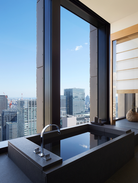 Aman Tokyo suite with floor-to-ceiling window framing Tokyo's skyline and a sleek black soaking tub.