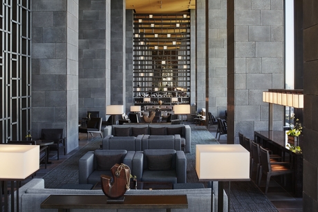 Aman Tokyo lounge with soaring stone walls, seating area, and illuminated shelving display.