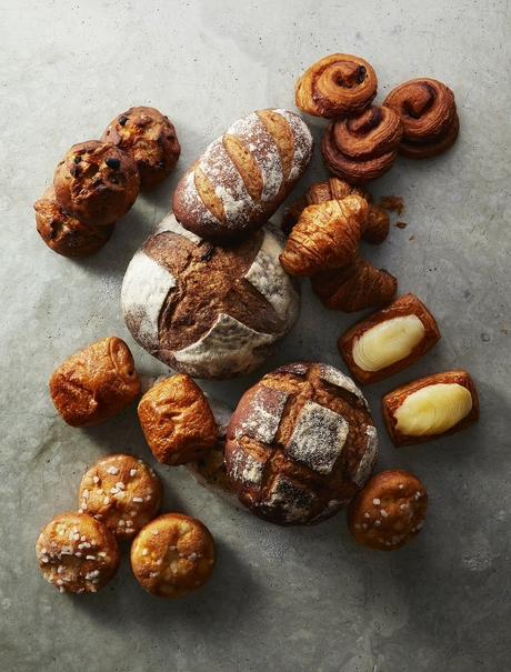 Assorted freshly baked pastries and bread from Aman Tokyo's patisserie, arranged on a grey surface.