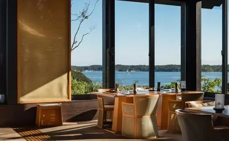 Espace de déjeuner à Amanemu avec vue panoramique sur la baie, mobilier en bois et lumière naturelle.