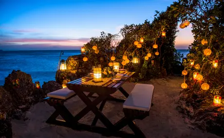Gary's Nest at Amanpulo resort: illuminated lanterns and loungers on a moonlit beach at dusk.