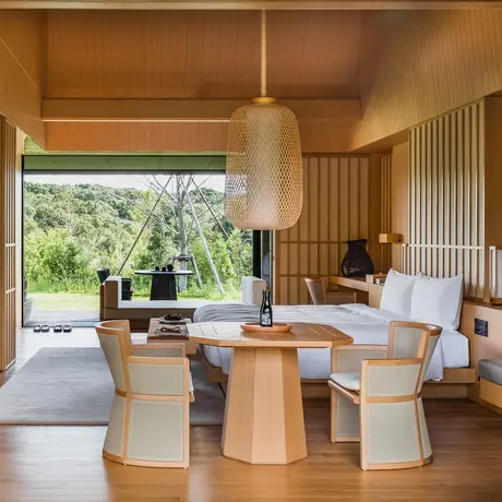Suite principale avec baie vitrée, mobilier en bois naturel et vue sur les jardins à Amanemu.