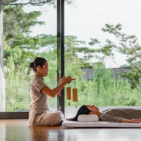 Wellness therapist performing a treatment on a guest at Amanemu resort, Japan, with views of forested landscape through expansive windows.