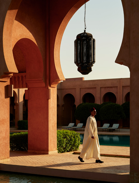 Woman walking through Moroccan arched corridor towards courtyard at Amanjena.