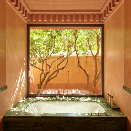 Sunlit plunge pool framed by arched doorway at Amanjena, with mature tree visible beyond.