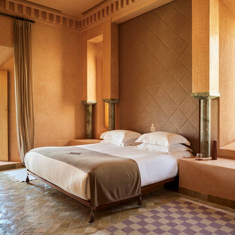 Principal bedroom at Amanjena with terracotta walls, geometric floor tiles, and draped bed linens.