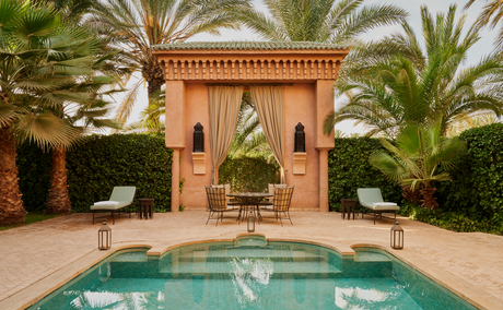 Courtyard with turquoise plunge pool at Amanjena, framed by terracotta arches and palm trees.