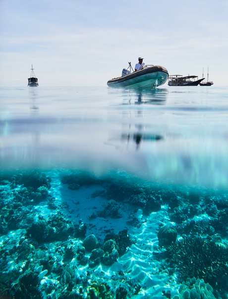 Diving boat Amandira anchored above a turquoise coral reef with clear waters.