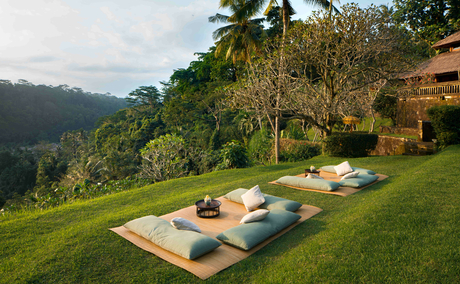 Sundowner picnic setup on a manicured lawn at Amandari, with cushioned seating arranged on the grass overlooking verdant valley views.