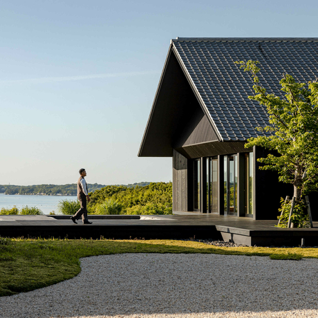 Modern black pavilion with pitched roof overlooking water at Amanemu resort, Japan.