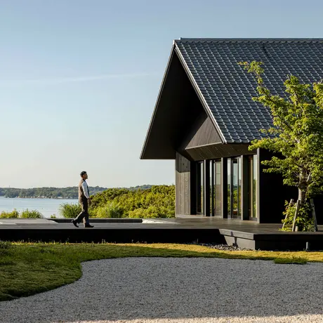 Amanemu resort pavilion with dark timber exterior overlooking water, surrounded by manicured gardens and stone pathway.