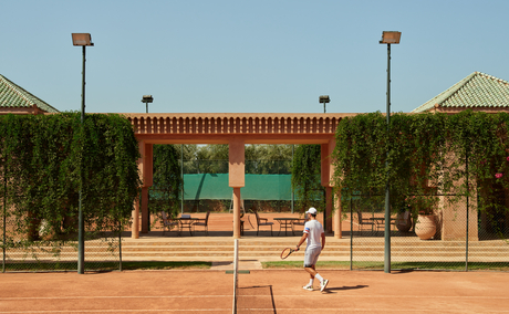 Amanjena tennis court with clay surface and ivy-covered pavilion backdrop.