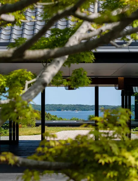 Amanemu resort exterior detail showing modernist architecture framed by verdant tree branches overlooking coastal landscape.