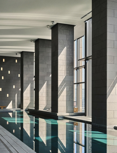 Tall marble columns line the edge of an indoor plunge pool at Aman Tokyo, their reflections mirrored in the still water below.