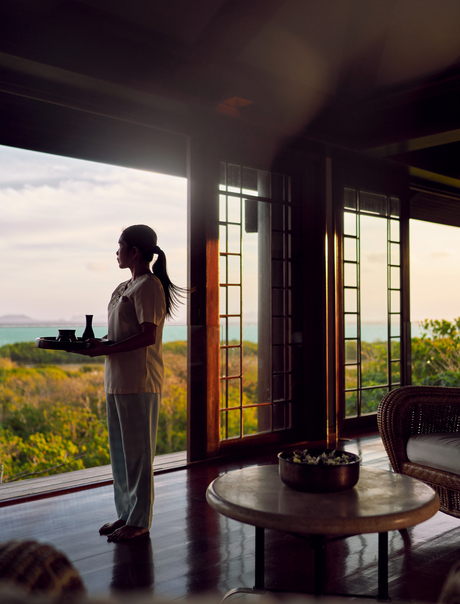 Woman standing at open doors gazing towards ocean view at Amanpulo spa and wellness retreat.