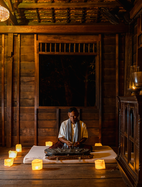 Woman meditating by candlelight in a wooden pavilion at Amansara, Cambodia.