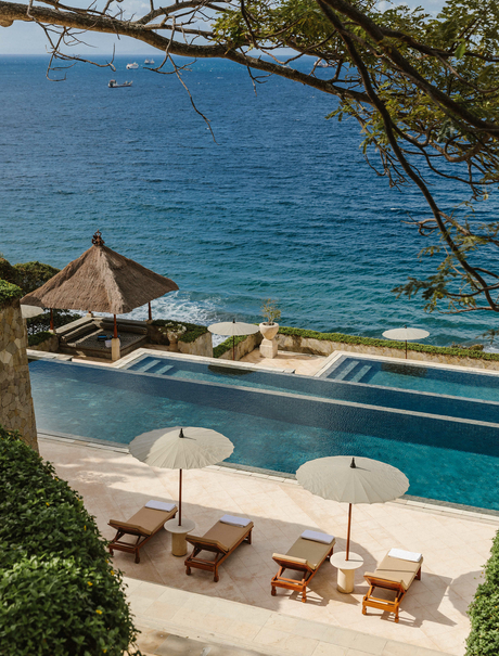 Amankila's portrait pool overlooking the ocean, with sun loungers and umbrellas on the terrace below.