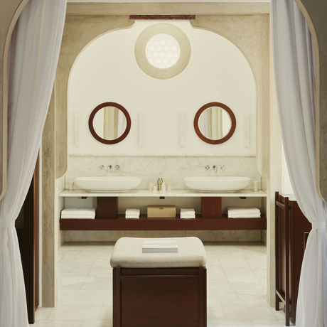 Amanruya deluxe sea view pavilion bathroom with dual circular mirrors and wooden vanity beneath arched ceiling.