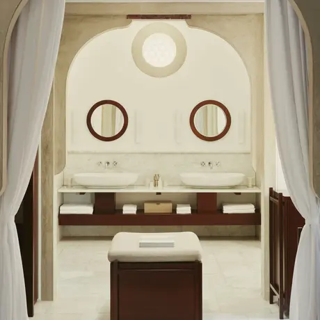 Amanruya deluxe sea view pavilion bathroom with dual circular mirrors and wooden vanity beneath arched ceiling.