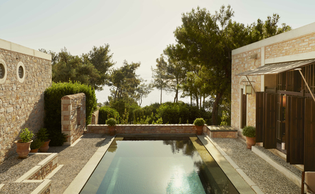Amanruya pavilion with rectangular plunge pool overlooking partial sea view, framed by stone walls and pine trees.