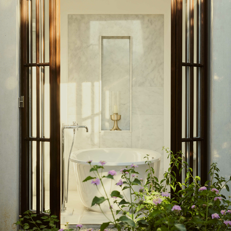 Amanruya pavilion bathroom with marble walls, brass fixtures, and potted plants framing the doorway.
