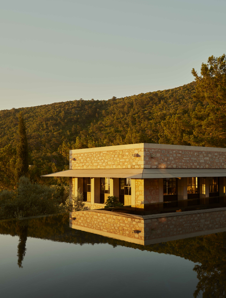 Amanruya's main pool and Ottoman lounge overlooking calm water at golden hour, surrounded by forested hillside.