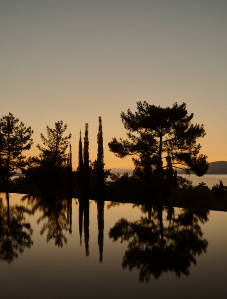 Silhouetted cypress and pine trees reflected in still water at Amanruya at sunset.