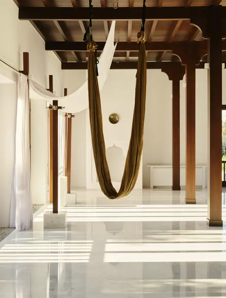 Aerial yoga swing suspended in a bright studio at Amanruya, with wooden beams and stone flooring.