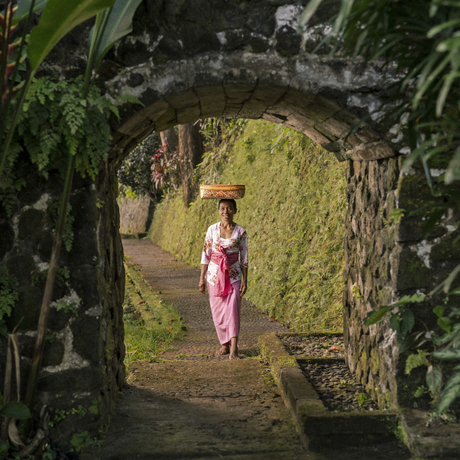 Woman in pink sarong walking through stone archway covered in moss at Amandari, Bali.