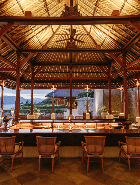 Amankila resort bar with timber-lined ceiling, wooden counter seating, and ocean views through large windows.