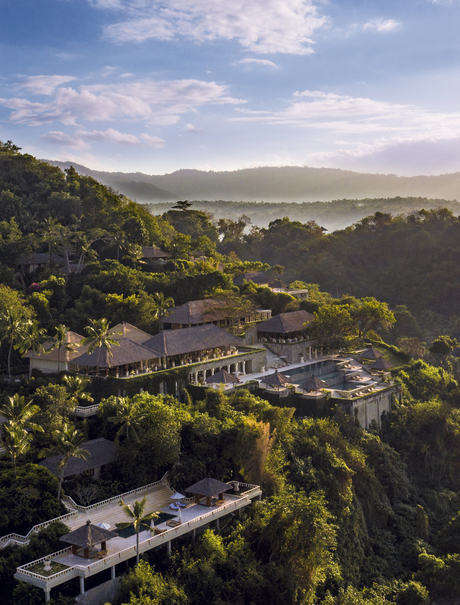 Amankila resort nestled amongst verdant hillsides overlooking coastal valley, aerial view.