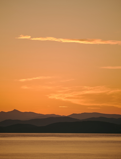 Sunset over calm waters with mountains silhouetted against an amber sky at Amanruya.