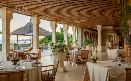 Amankila resort terrace with wooden beamed ceiling, dining tables, and views of surrounding landscape.