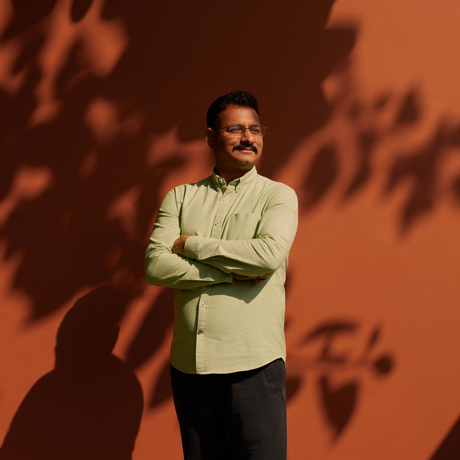 Aman-i-Khas General Manager Aman stands against a terracotta wall, arms crossed, with dappled shadows cast across the surface.